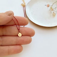 A very delicate necklace featuring double red thread strands, tiny golden nuggets on the sides and a round simple shape pendant.The pendant is custom stamped with the letter of your choice. Please, type the letter you want to be stamped on your pendant at check-out!∙ Only 1 letter permitted.∙ We use only capital letters.In many cultures, the color red is traditionally used as a symbol of protection, good luck, or blessing. In my native Argentina, red-is used to ward off evil spirits. Wear this n Valentine's Day Necklace With Delicate Round Pendant, Red Necklace With Charms And Round Pendant, Red Round Pendant Necklace, Dainty Red Round Pendant Necklace, Red Engraved Round Pendant Jewelry, Golden Nugget, Thread Necklace, Round Necklace, Neck Piece