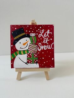 a small easel with a snowman painted on it and the words let it snow