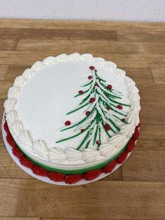 a white cake with green and red decorations on it sitting on a wooden table next to a knife