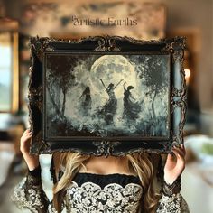 a woman is holding up a painting in front of her face with the moon behind her