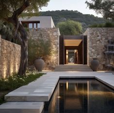 an outdoor swimming pool surrounded by stone walls and water features at the entrance to a modern home