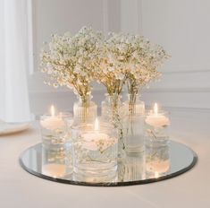 flowers and candles are arranged in glass vases on a table with a mirror plate