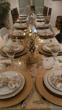 the table is set for christmas dinner with white and gold plates, silverware, and napkins