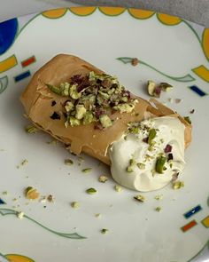 a piece of cake on a plate with whipped cream and pistachio toppings