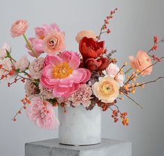 a white vase filled with lots of pink and orange flowers