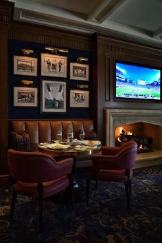 two red chairs sitting at a table in front of a fireplace with pictures on the wall