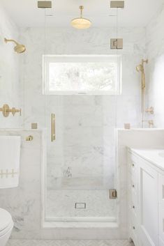 a white bathroom with gold fixtures and marble tile flooring, along with a walk in shower