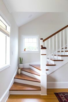 a white staircase with wooden handrails leading up to the second floor and window