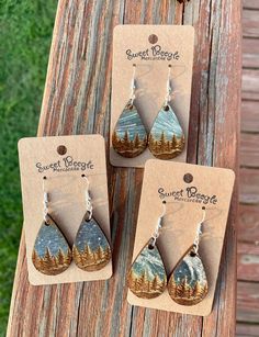 three earrings with trees on them sitting on top of a piece of wood next to each other