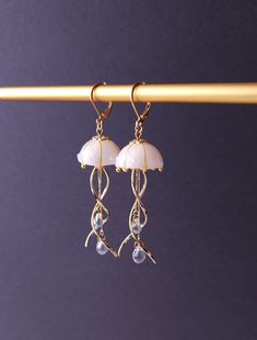 Introducing our stunning Jellyfish Earrings, crafted with utmost care and fashioned with a unique blend of resin, curved metal charms, and delicate teardrop beads. These enchanting earrings capture the graceful movement of jellyfish in a captivating design that is sure to turn heads. Each intricately detailed jellyfish is meticulously molded from resin, showcasing their ethereal beauty. The curved metal charms add a touch of elegance and whimsy, perfectly complemented by the shimmering teardrop Whimsical White Resin Jewelry, Whimsical Resin Jewelry With Ear Wire, Whimsical Resin Dangle Earrings, White Jelly Fish, Jellyfish Jewelry, Jellyfish Earrings, Ethereal Jewelry, Graceful Movement, Bracelet Inspo