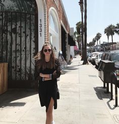 a woman walking down the sidewalk in front of a building with palm trees on both sides