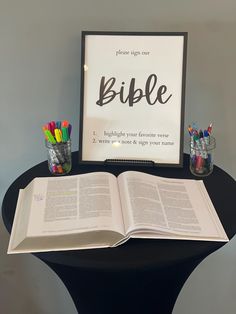 an open bible sitting on top of a table next to pencils and cups with pens