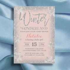 a pink and silver winter wonderland baby shower is displayed on a light blue satin background