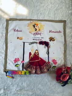 a doll sitting on top of a white blanket next to a red rose and some flowers