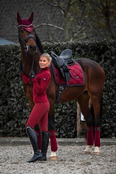 a woman standing next to a brown horse in front of a hedged area with bushes