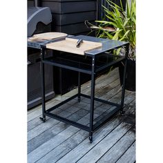 a black table with a wooden cutting board on it and some plants in the background