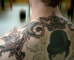 the back of a man with tattoos on his neck and shoulder, wearing a top hat