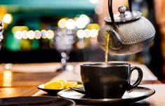 a teapot pouring water into a cup on top of a plate with lemon wedges