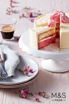 a white cake with pink frosting on a plate next to a cup of coffee