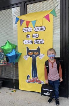 a young boy standing in front of a bulletin board with a black cat on it