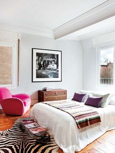 a bedroom with a zebra rug, pink chair and white bed in the corner next to a window