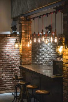 several lights hanging from the ceiling in a brick walled room with stools and tables