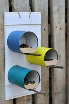 two blue and yellow bird feeders hanging on a wooden fence next to each other