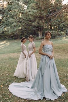 three bridesmaids standing in the grass with their dresses draped down and looking at each other