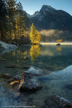 a lake surrounded by mountains and trees in the middle of it with mist coming from the water