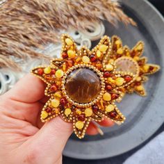 a person is holding two brooches in their hand and one has a brown stone on it