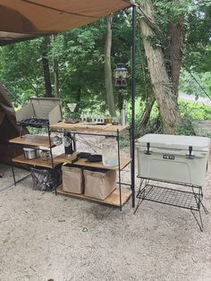 an outdoor cooking station with coolers and other items under a tent in the woods