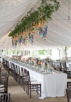 the tables are set up with white linens and floral centerpieces hanging from the ceiling