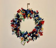 an origami wreath hanging on the wall in front of a white wall with red, blue and green decorations