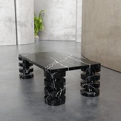 a black marble table sitting on top of a floor next to a potted plant