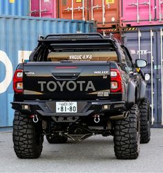 the back end of a black toyota truck parked in front of some shipping containers on display