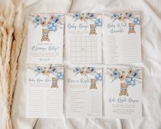 four baby shower games with teddy bears and blue flowers on them, laid out on a bed