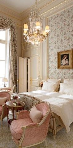 a bedroom with floral wallpaper, chandelier and pink chairs in front of the bed