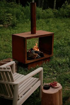 a fire pit sitting in the middle of a lush green field next to two white chairs