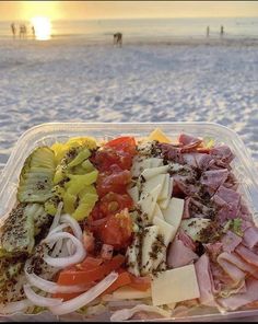 a plastic container filled with lots of food on top of a beach next to the ocean