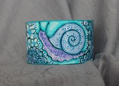 A bright turquoise image of a snail on a wide, steel The bracelet framed with pebbles and flowers is made with special acrylic paints. Colors of summer holidays and sea surf. Carefree and joyful is the theme of this bracelet. The bracelet provided is the original work of artist Polina Yurekli. This bracelet is perfect as a gift for yourself or for a special friend. It is suitable for a woman who is not afraid to stand out from the crowd. My bracelets will not only decorate your look, but will al Unique Hand Painted Cuff Bracelet As Gift, I Wish You Happiness, Colors Of Summer, Steel Paint, Bright Turquoise, Acrylic Pour, Summer Holidays, Special Friend, Acrylic Paints