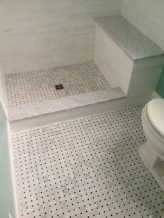 a white toilet sitting inside of a bathroom next to a walk in shower stall on top of a tiled floor