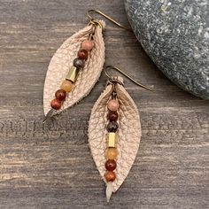 two leaf shaped earrings with beads hanging from them on top of a wooden table next to a rock