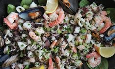 a bowl filled with shrimp, mussels and lemon wedges on top of a table