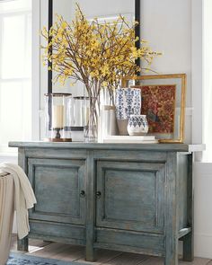 a vase with yellow flowers sitting on top of a wooden cabinet next to a mirror