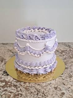 a three tiered cake with purple ruffles and gold trim on a table