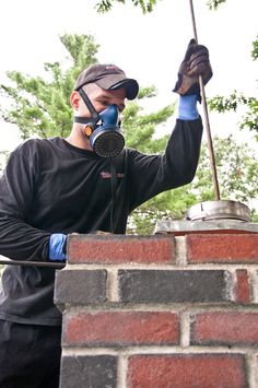 a man wearing a gas mask and holding a broom in front of a brick wall