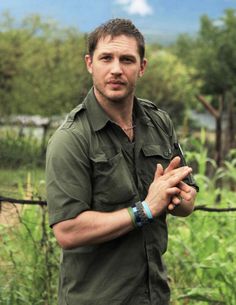 a man standing in front of a fence with his hands together and looking at the camera