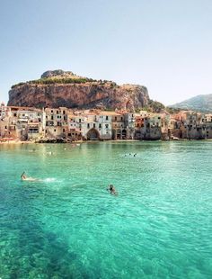 people are swimming in the clear blue water next to an island with houses on it