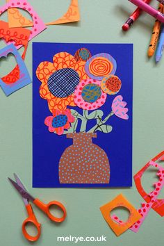 an art project with scissors and paper flowers in a vase on a blue background surrounded by cut outs