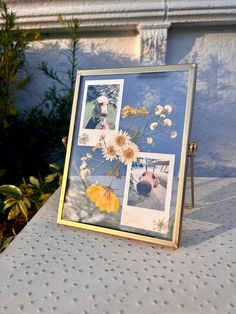 a photo frame with pictures and flowers on it sitting on a table next to potted plants